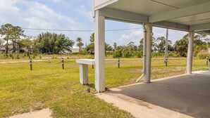 A covered outdoor area with a concrete bench, chain-link fence, and grassy surroundings. - Sandbag Castle 4bdr Waterfront (Orange Beach)
