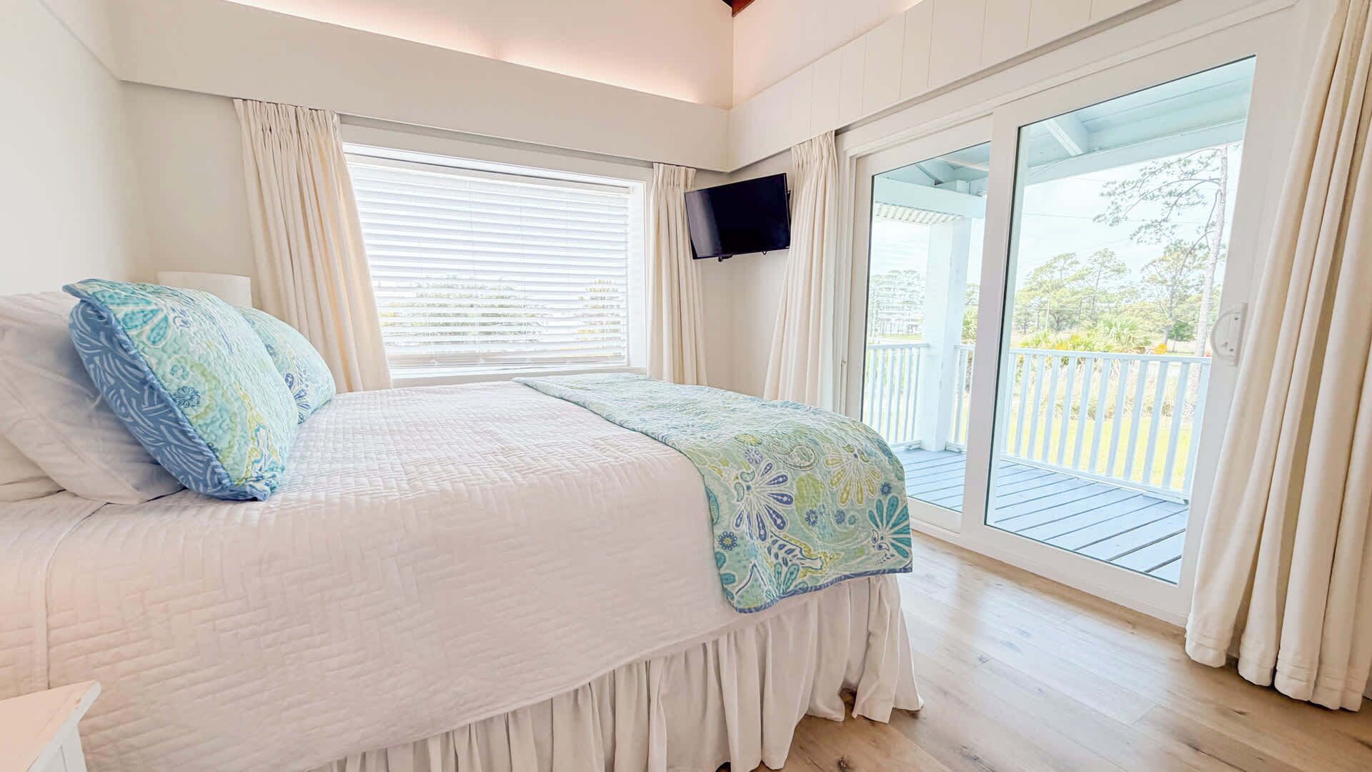 A bedroom with a bed, a TV, and a balcony with a view.