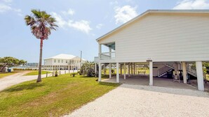 A coastal building with a covered outdoor area, a palm tree, and a clear sky. - Sandbag Castle 4bdr Waterfront (Orange Beach)