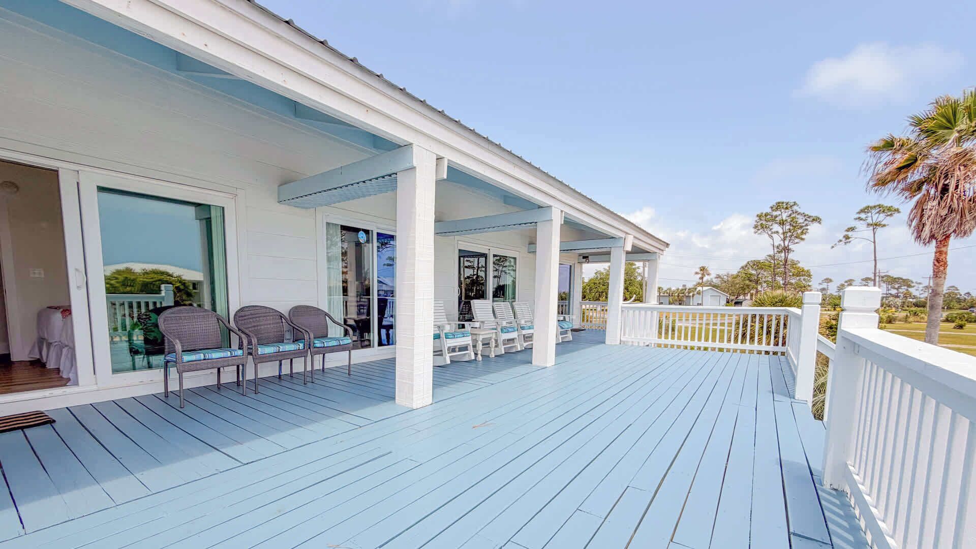 A covered outdoor area with white railings, a blue deck, and wicker chairs.