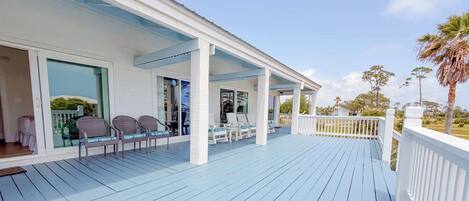 A covered outdoor area with white railings, a blue deck, and wicker chairs.
