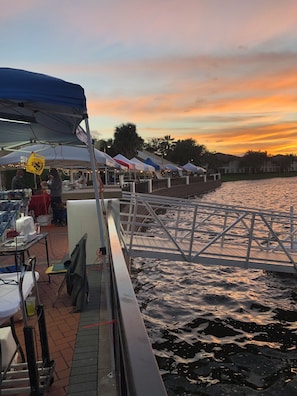 A waterfront market with tents and tables, a dock, and a sunset view.