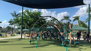 Un parque infantil con una estructura para escalar, bancos y una zona de estar cubierta.