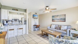 Un espacio habitable compacto con kitchenette, comedor y zona de estar con sofá y mesa de centro.