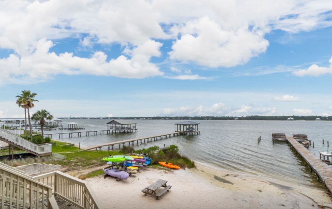 Une plage avec une jetée en bois qui s’avance dans une eau calme, une rangée de kayaks aux couleurs vives et un petit pavillon.