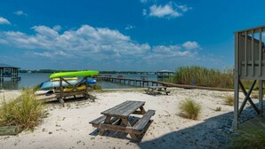 Una playa con un muelle de madera, una mesa de picnic y canoas.