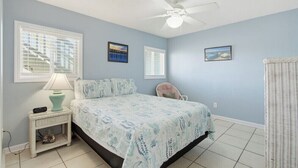 Un dormitorio con cama, mesita de noche, lámpara, sillón y ventilador de techo.