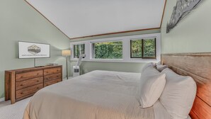 Ein Schlafzimmer mit Bett, Kommode und einem Fenster mit Blick auf Grünflächen.
