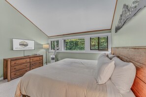 Ein Schlafzimmer mit Bett, Kommode und einem Fenster mit Blick auf Grünflächen.