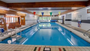 Ein Hallenbad mit klarem Wasser, Holzbalken an der Decke und einem gefliesten Boden.