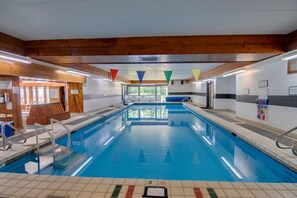 Ein Hallenbad mit klarem Wasser, Holzbalken an der Decke und einem gefliesten Boden.