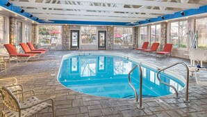 Une piscine intérieure dotée d’un sol en pierre, de chaises longues rouges et d’un plafond avec des poutres blanches.