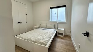 Un dormitorio con cama, mesitas de noche, ventana y armario.