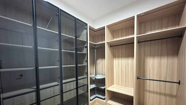 Una habitación con armario de vidrio, estantería de madera y un mueble de esquina.