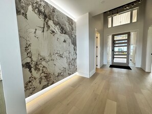 Ein Flur mit einer großen, strukturierten Wand, Holzboden und einer Tür zu einem anderen Raum.