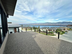 A residential area with houses, a street, and a body of water in the distance. - The Malbec Residence: Live Luxury with your Favourite People! (West Kelowna)