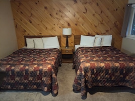 Una habitación con dos camas, una mesita de noche con lámpara y una pared de madera.