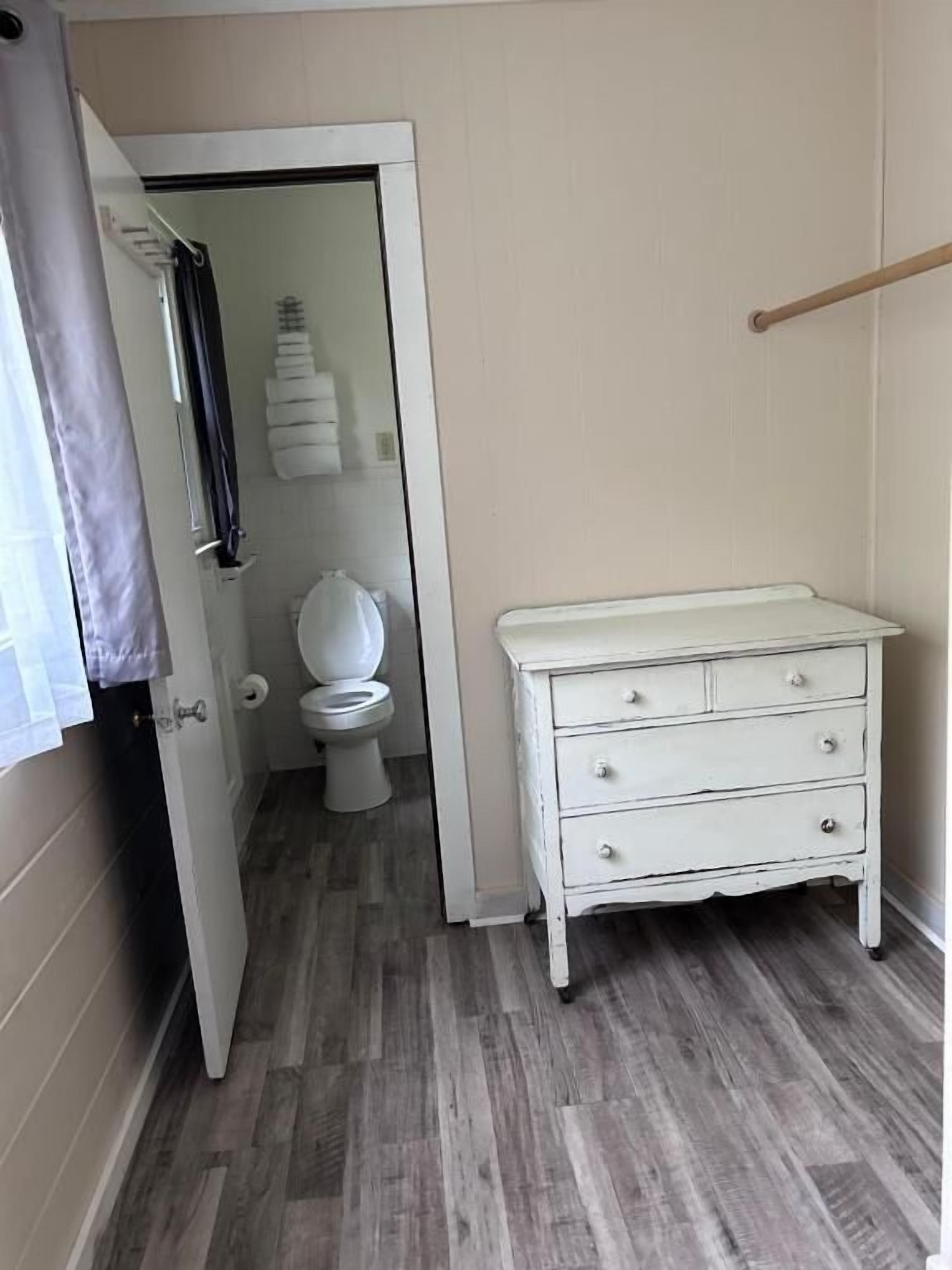 A bathroom with a toilet, a white cabinet, and a wooden floor.