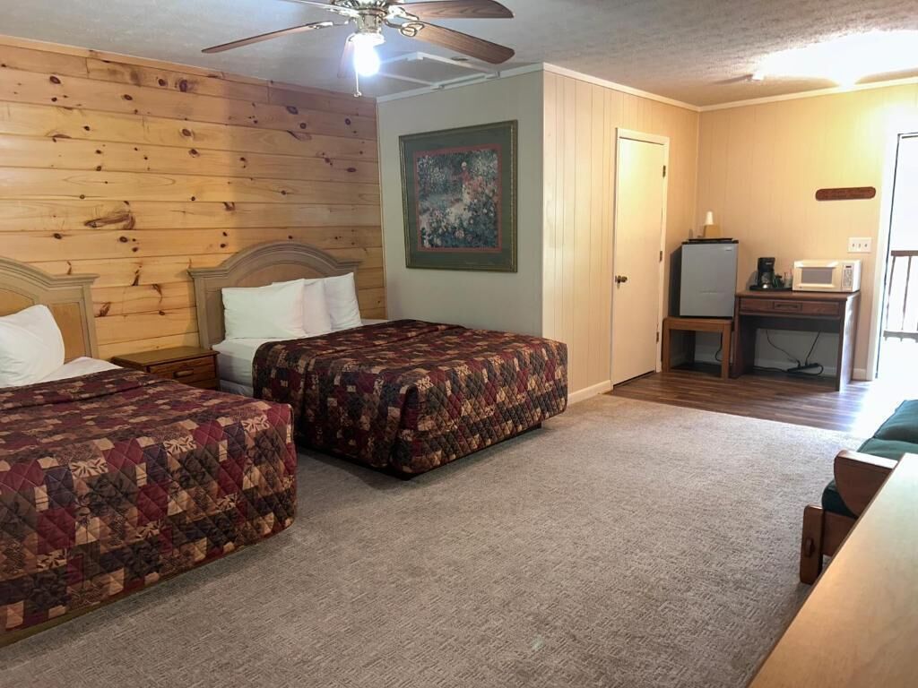 A bedroom with two beds, a ceiling fan, a painting, a desk with a computer, and a microwave.