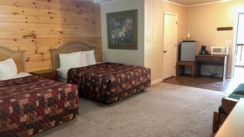 A bedroom with two beds, a ceiling fan, a painting, a desk with a computer, and a microwave.