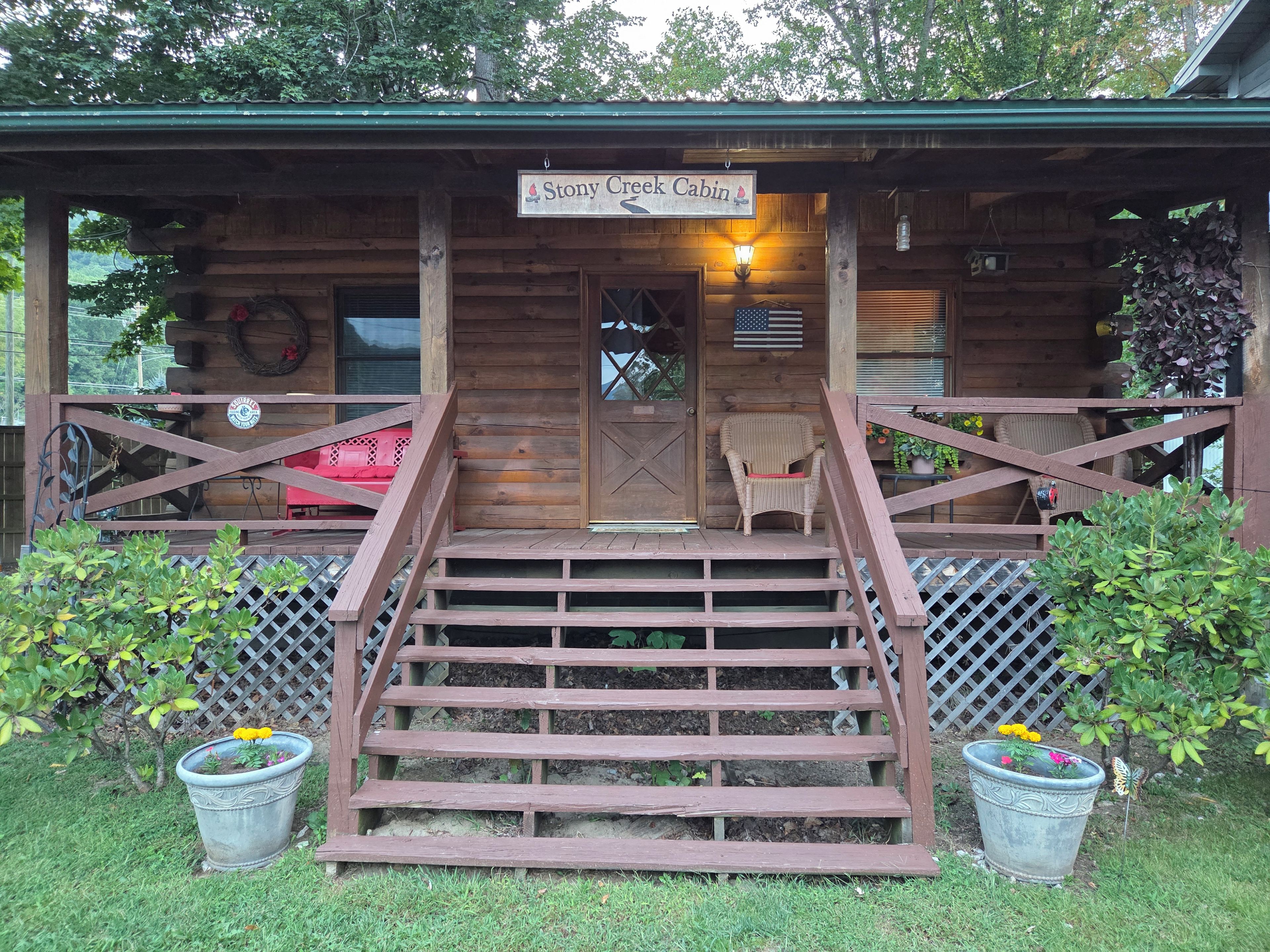 A wooden cabin with a porch, a staircase leading to the entrance, and potted plants.