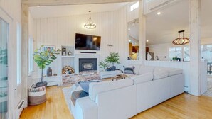 Uma sala de estar espaçosa com um sofá branco grande, uma lareira e uma televisão.