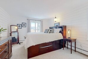 Un dormitorio con cama, cómoda, espejo, mesita de noche, lámpara y ventana con cortinas.