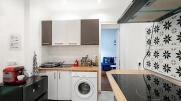 A compact kitchen with a washing machine, a coffee maker, and a dining area with a black induction cooktop.