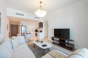 A modern living room with a sofa, coffee table, TV, and a kitchen area in the background. - Elegant 1BR Apt, Steps Away from Dubai Mall (Dubai)