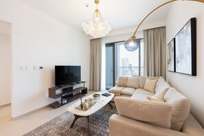 A modern living room with a flat-screen TV, a sofa, a coffee table, and a chandelier. - Elegant 1BR Apt, Steps Away from Dubai Mall (Dubai)