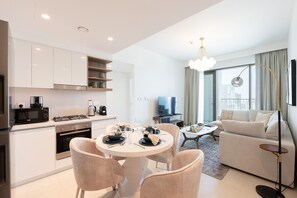 A modern living room with a sofa, a dining table set for four, and a kitchen area with a stove and microwave. - Elegant 1BR Apt, Steps Away from Dubai Mall (Dubai)
