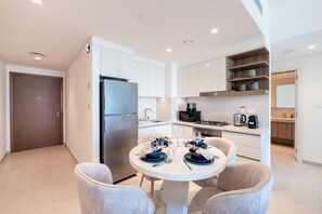 A modern kitchen with white cabinets, a stainless steel refrigerator, and a dining area with a round table and two chairs. - Elegant 1BR Apt, Steps Away from Dubai Mall (Dubai)