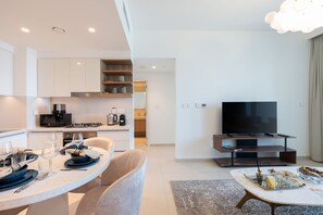 A modern living room with a flat-screen TV, a dining area with a table set for two, and a kitchen with built-in appliances. - Elegant 1BR Apt, Steps Away from Dubai Mall (Dubai)