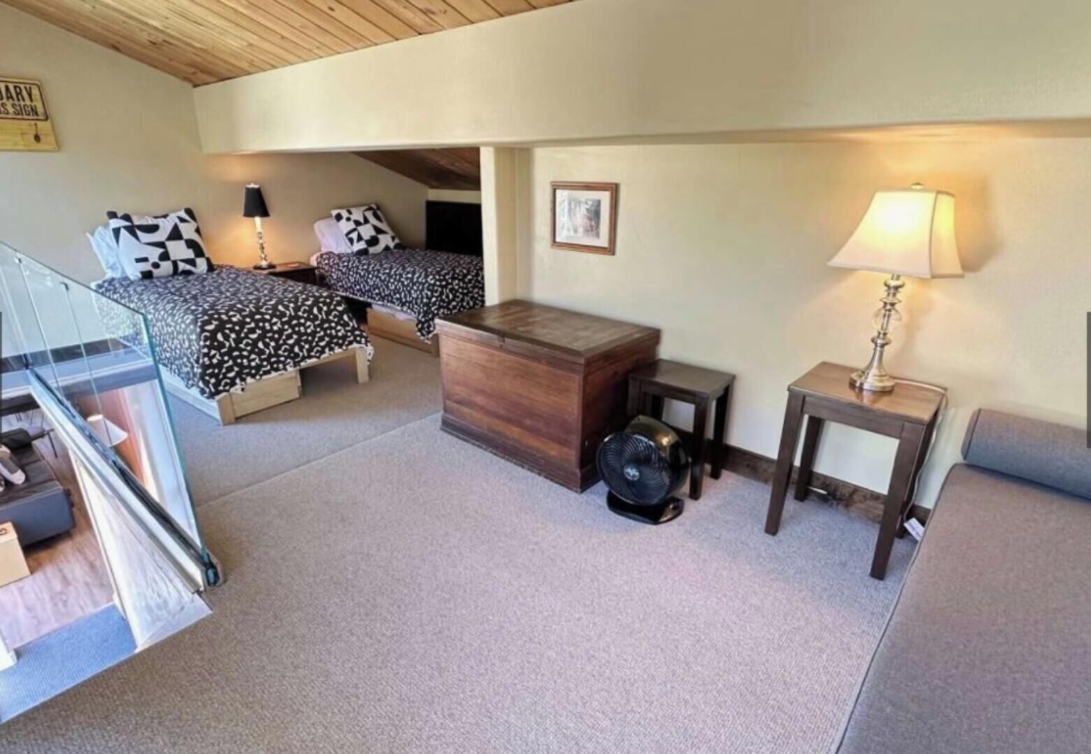 A bedroom with two beds, a wooden dresser, a fan, a lamp, and a framed picture on the wall.