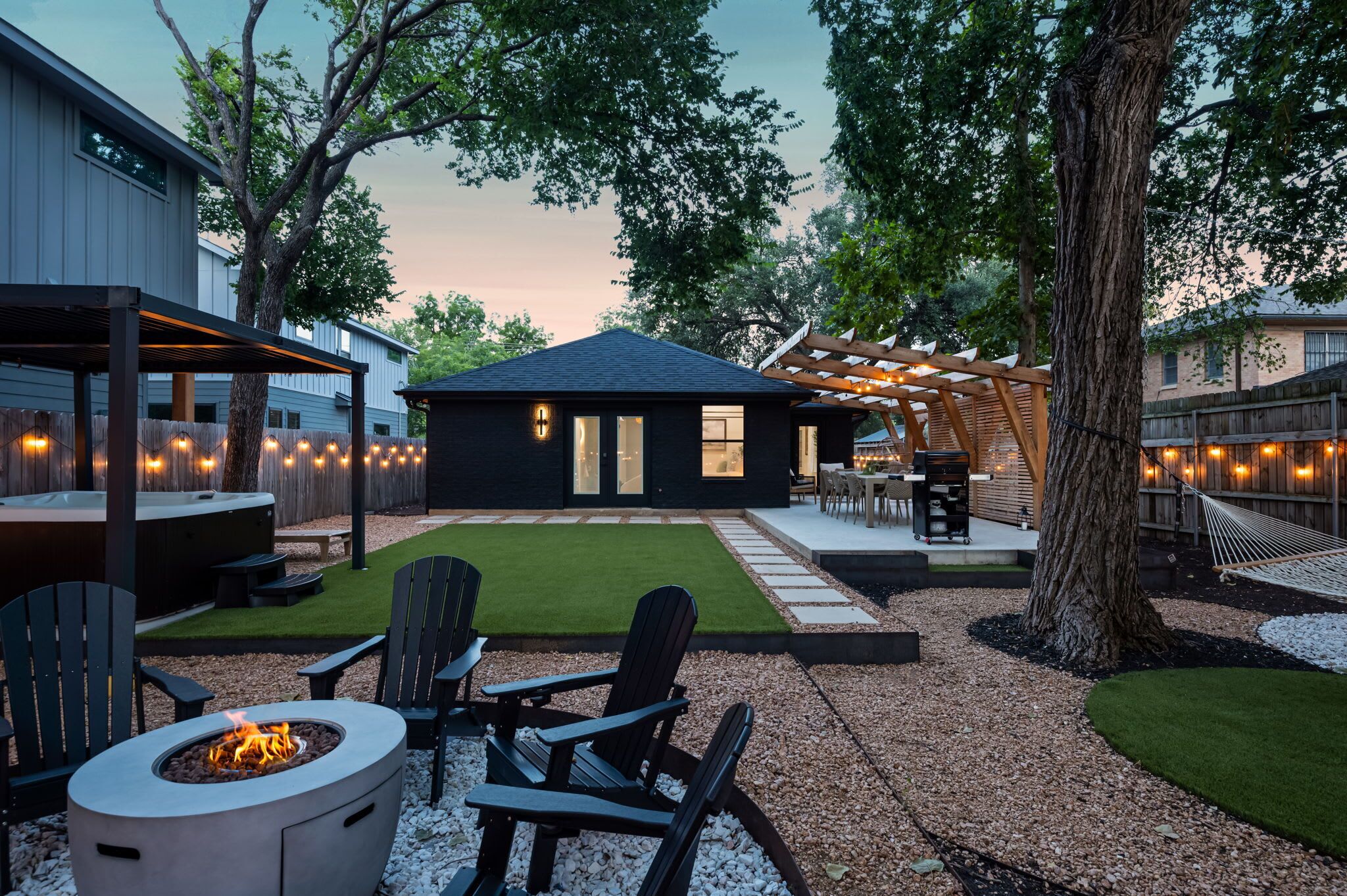 A backyard with a fire pit, outdoor seating, a hot tub, and a covered patio area.