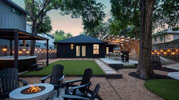Un jardin avec un foyer, des sièges d’extérieur, un jacuzzi et un patio couvert.