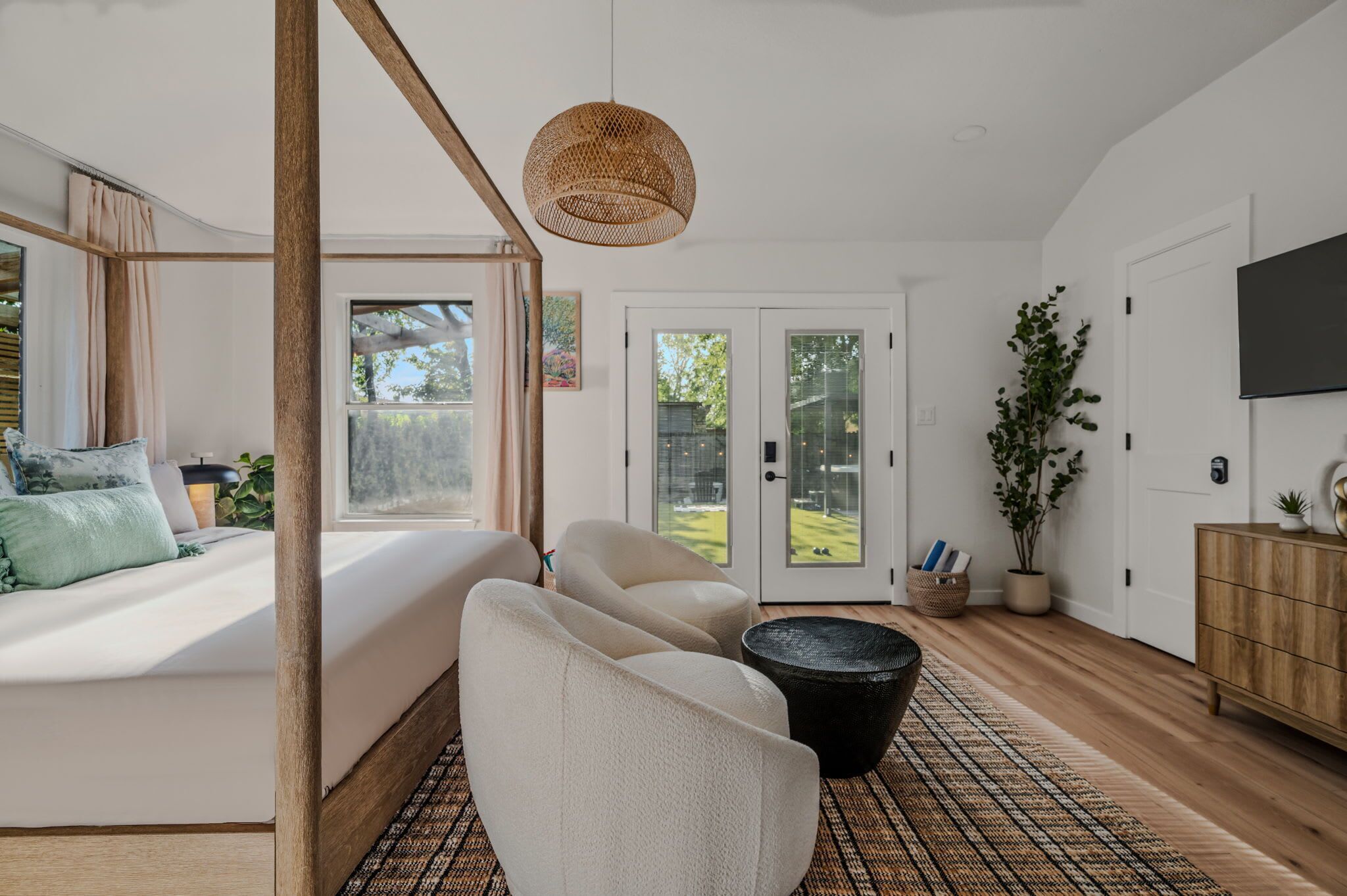 Une chambre dotée d’un grand lit, d’un coin salon avec des fauteuils, d’un luminaire en fibres tressées, d’une télévision et offrant une vue sur l’extérieur grâce à des portes vitrées.
