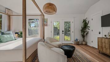 Une chambre dotée d’un grand lit, d’un coin salon avec des fauteuils, d’un luminaire en fibres tressées, d’une télévision et offrant une vue sur l’extérieur grâce à des portes vitrées.