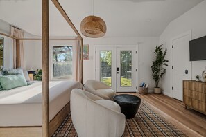 A bedroom with a large bed, a sitting area with chairs, a woven light fixture, a television, and a view of the outdoors through glass doors. - Onyx & Oak - Hot Tub & Backyard Oasis, East Austin (Austin)