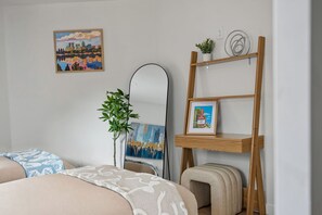 A hotel room with a bed, a mirror, a small wooden shelf with a picture, a plant, and a painting on the wall. - Onyx & Oak - Hot Tub & Backyard Oasis, East Austin (Austin)