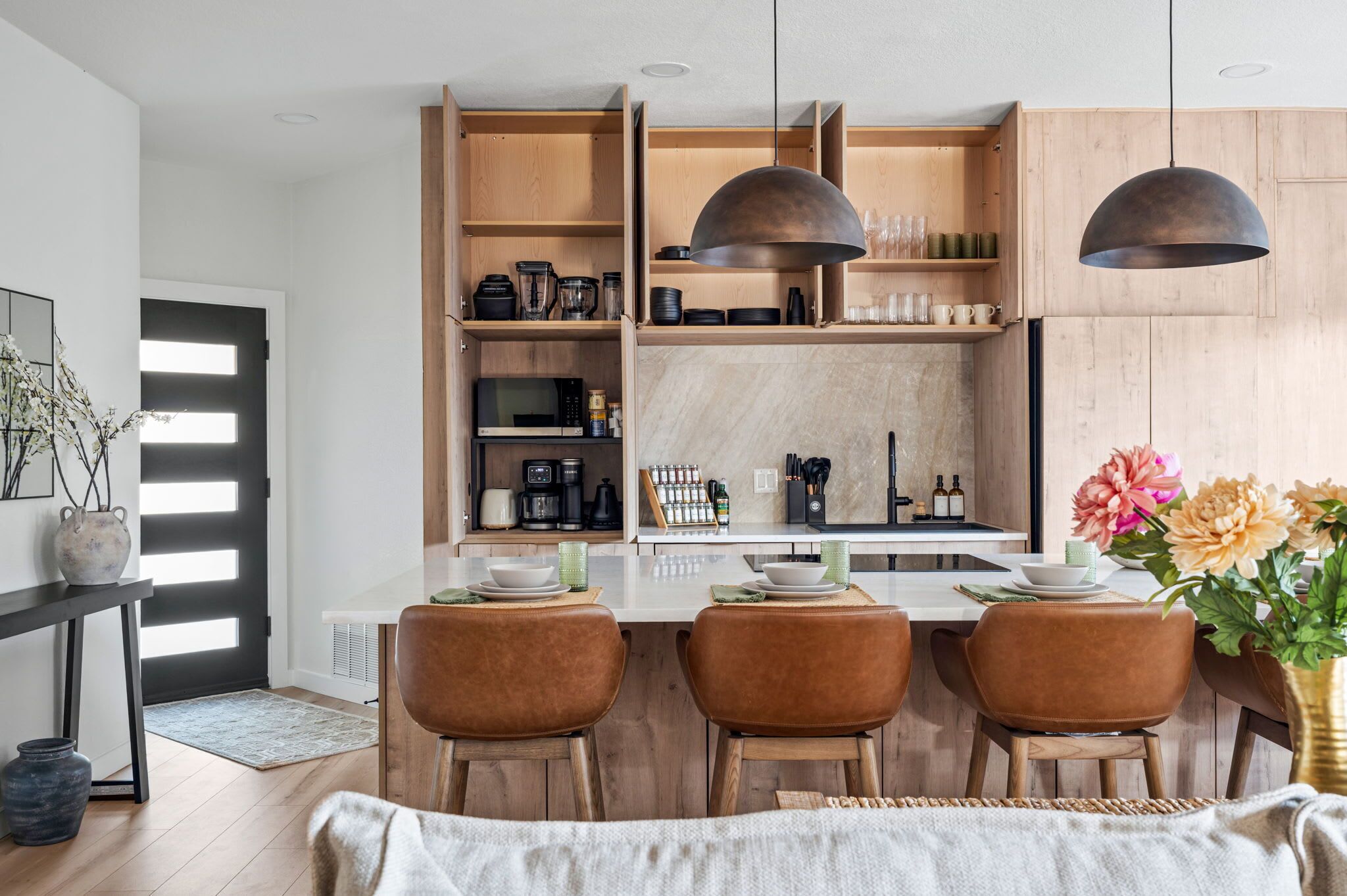 Une cuisine moderne avec des meubles en bois, un îlot central doté de sièges, un éclairage suspendu et un coin repas avec des chaises.