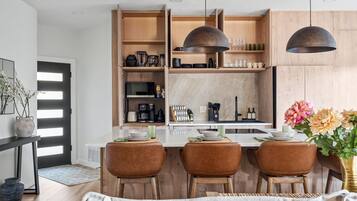 Une cuisine moderne avec des meubles en bois, un îlot central doté de sièges, un éclairage suspendu et un coin repas avec des chaises.