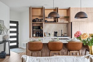 A modern kitchen with wooden cabinets, a central island with seating, pendant lighting, and a dining area with chairs. - Onyx & Oak - Hot Tub & Backyard Oasis, East Austin (Austin)