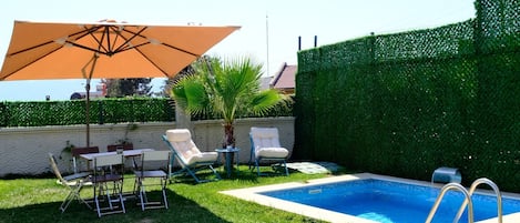 Un jardin avec une piscine, un coin repas avec des chaises et une table, et un grand parasol.