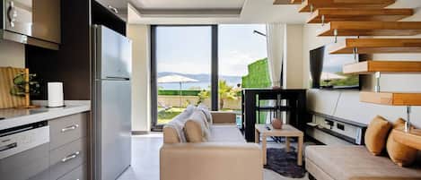 A modern kitchen with a built-in refrigerator, a dining area with a sofa and a TV, and a large sliding glass door leading to a balcony with a view.