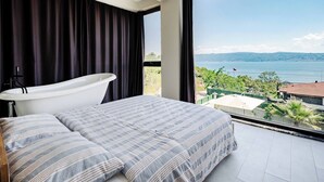 A bedroom with a large window, a bathtub, and a bed with striped bedding. - 4-deluxe Villa With Heated Private Pool (Dilovasi)