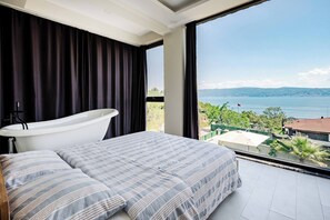 A bedroom with a large window, a bathtub, and a bed with striped bedding. - 4-deluxe Villa With Heated Private Pool (Dilovasi)