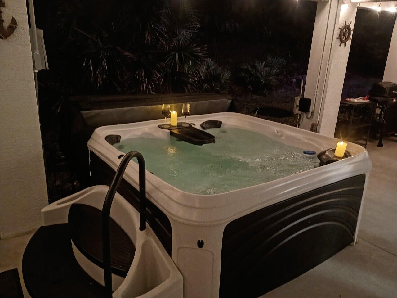 A hot tub with two candles, a chair, and a small table.
