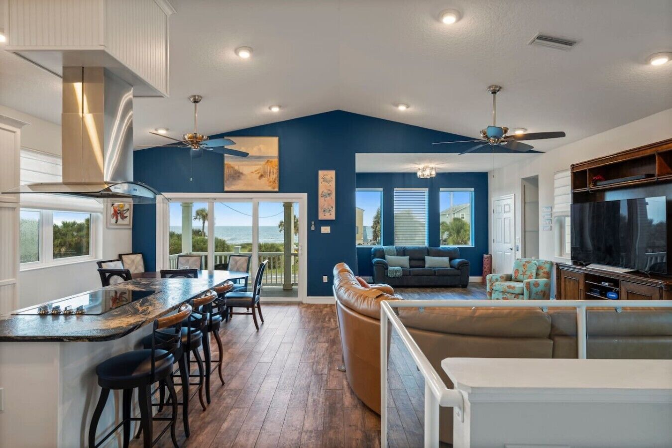A spacious living area with a large TV, a dining area with bar stools, and a view of the ocean.