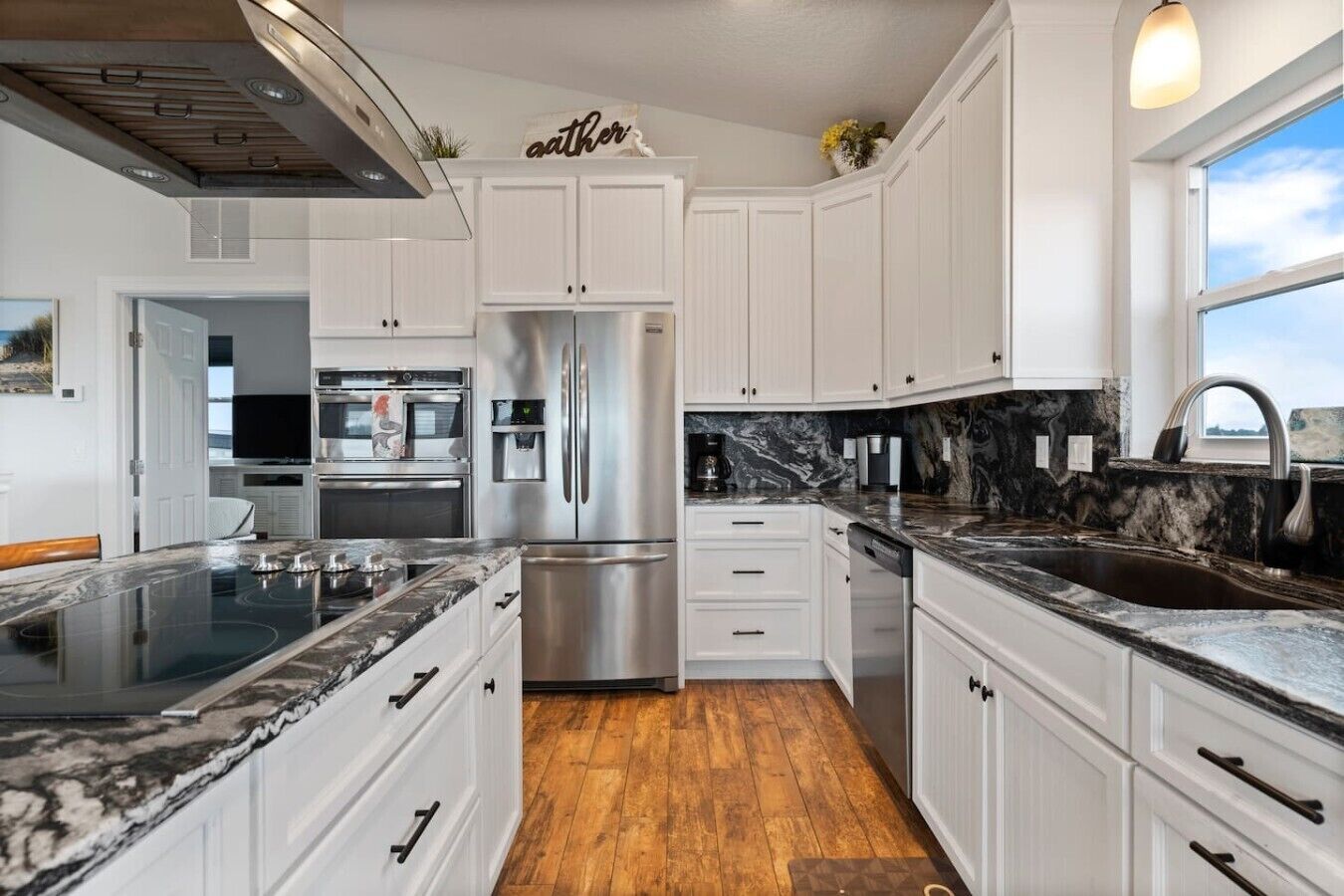 Una cocina moderna con armarios blancos, electrodomésticos de acero inoxidable, encimera de mármol y suelo de madera.